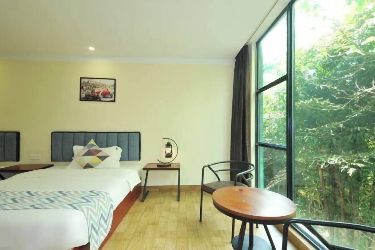 Habitación de hotel con cama, mesita de noche, silla y ventana con vistas al verdor.