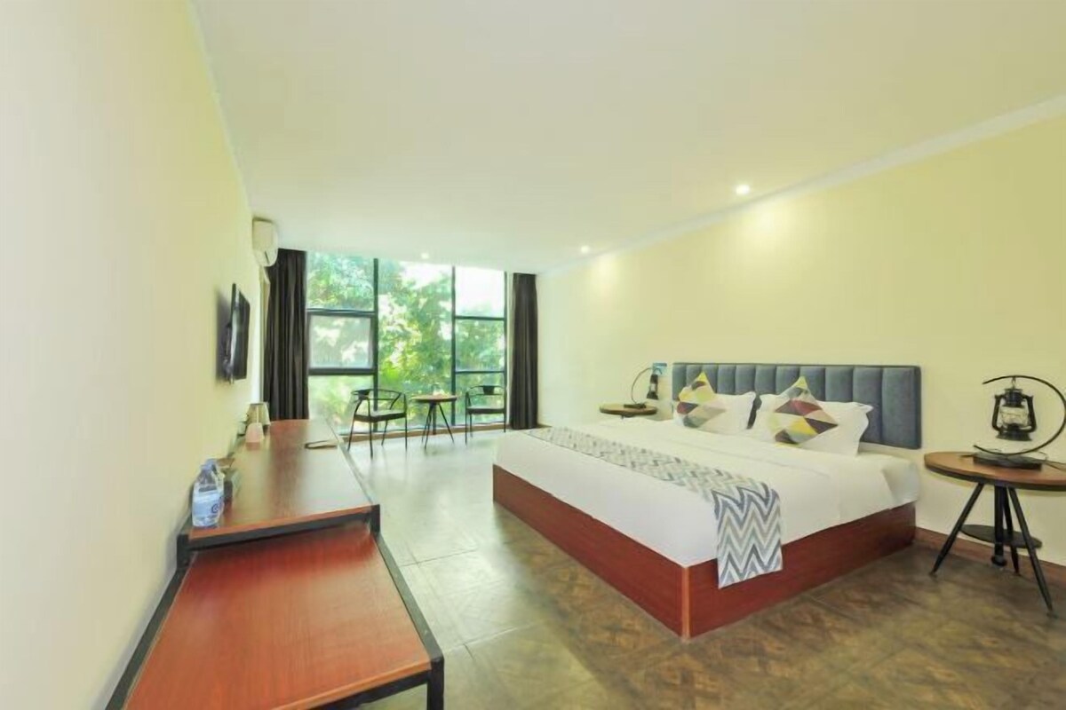 Habitación de hotel con una cama grande, un escritorio y una silla. Se ve una ventana con vistas a árboles.