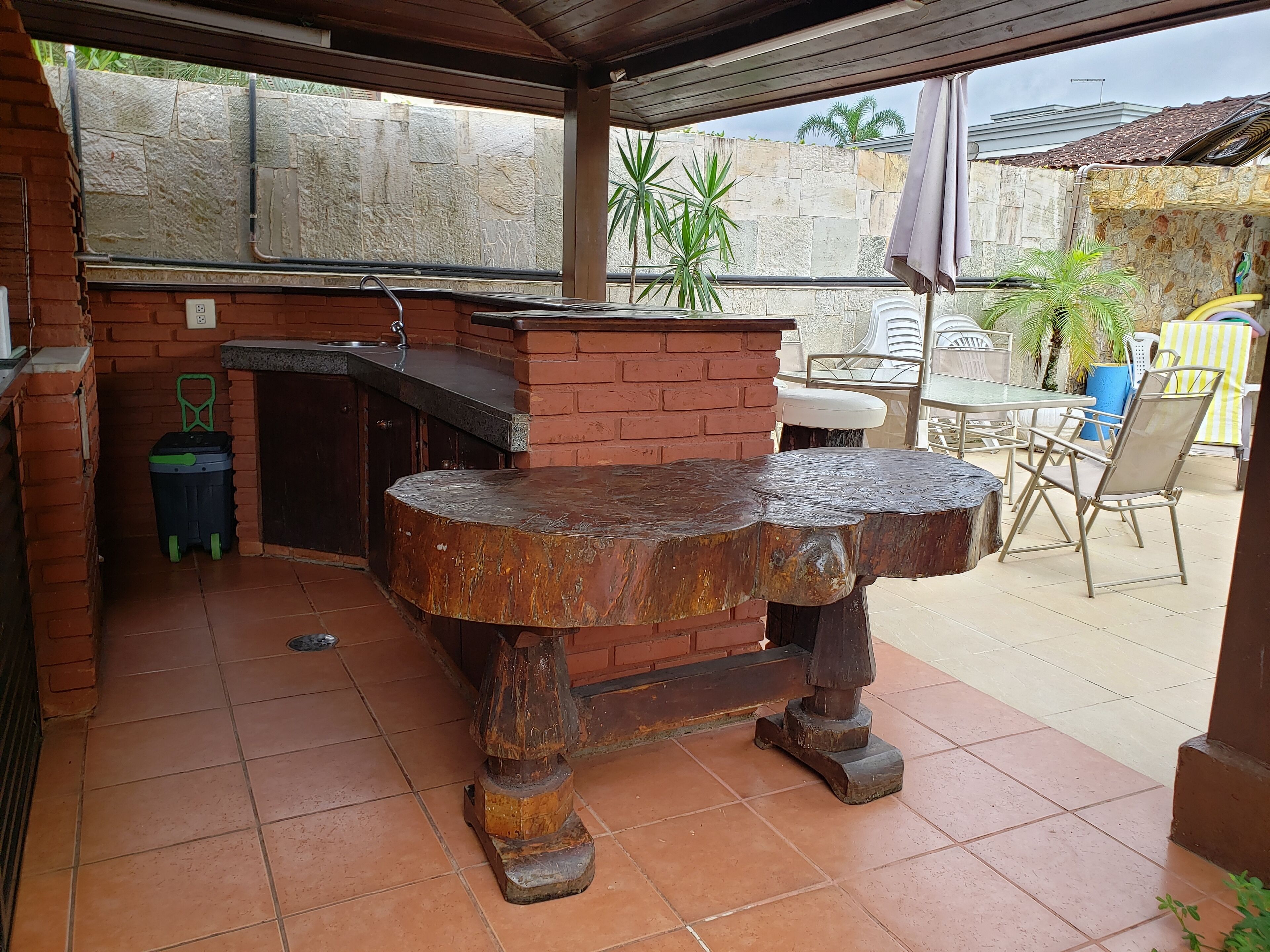 A rustic outdoor kitchen with a brick counter and a large wooden table.