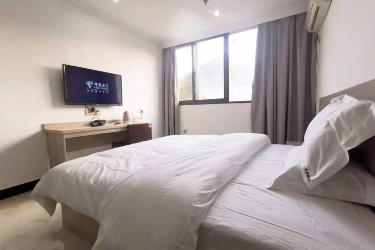 Habitación de hotel con cama, escritorio, televisión de pantalla plana y ventana con cortinas.