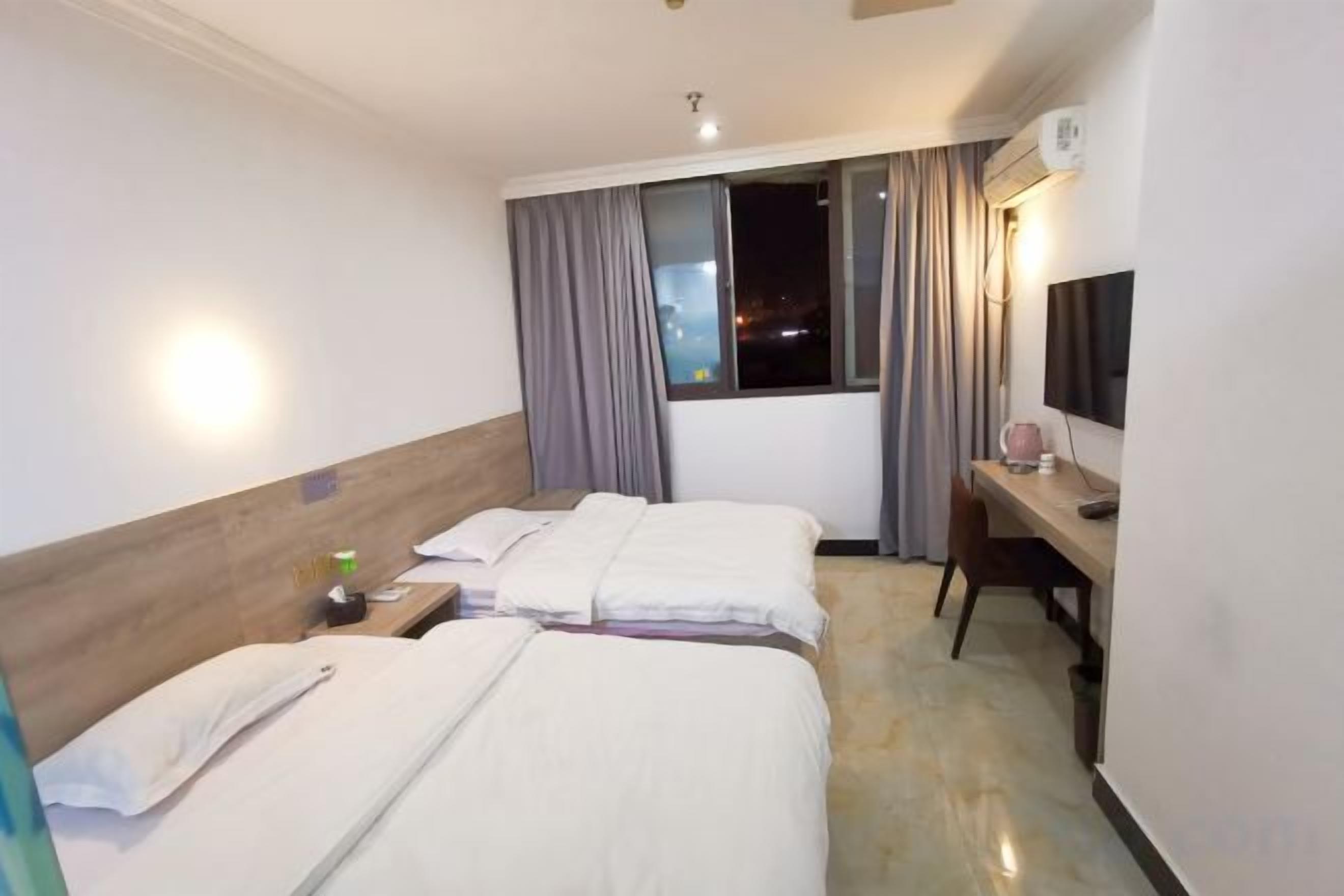 A hotel room with two beds, a desk, a chair, a TV, and a window with curtains.