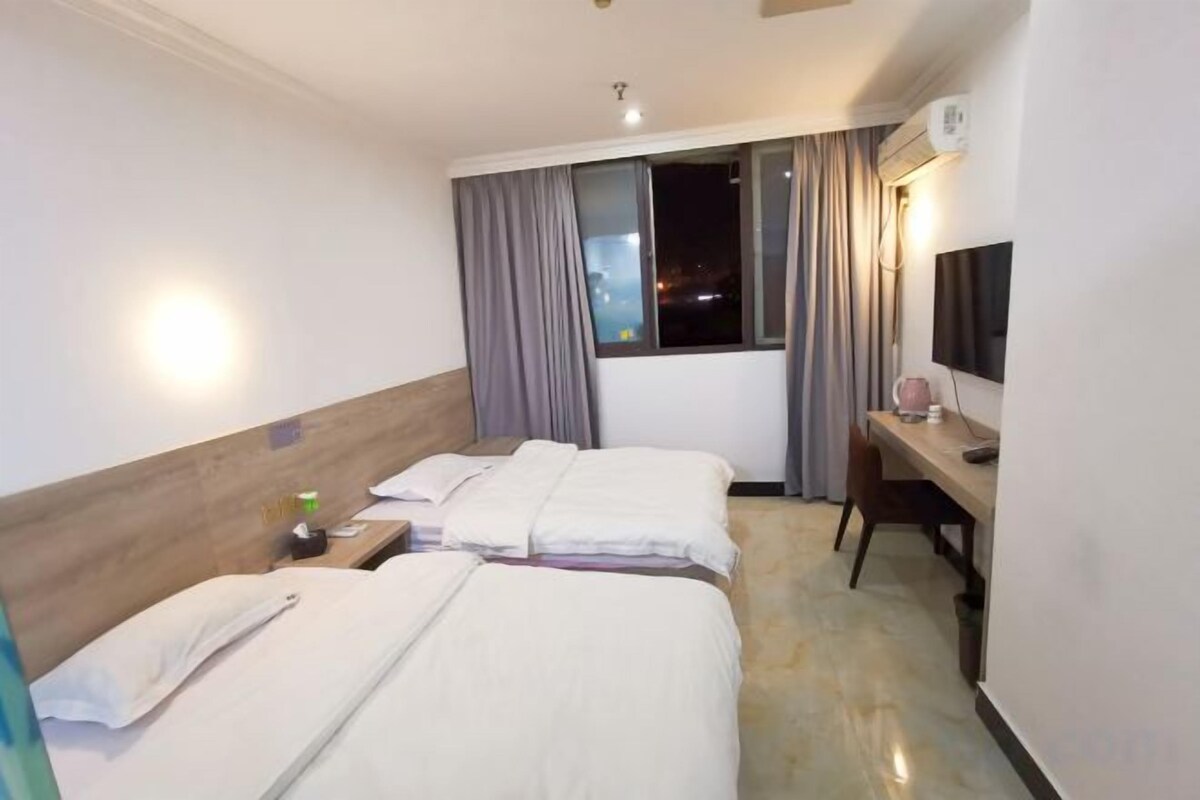 A hotel room with two beds, a desk, a chair, a TV, and a window with curtains.