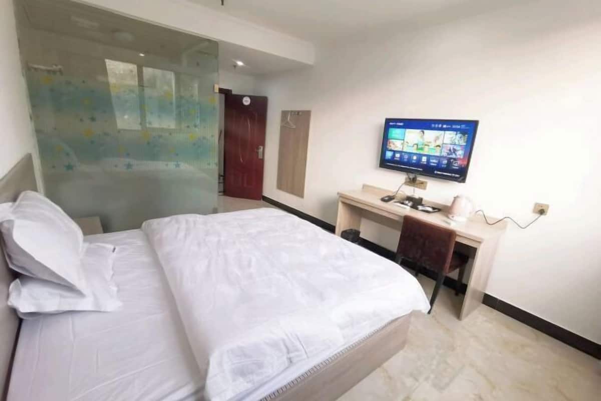 Una habitación de hotel con cama, escritorio, televisor y un separador de vidrio.
