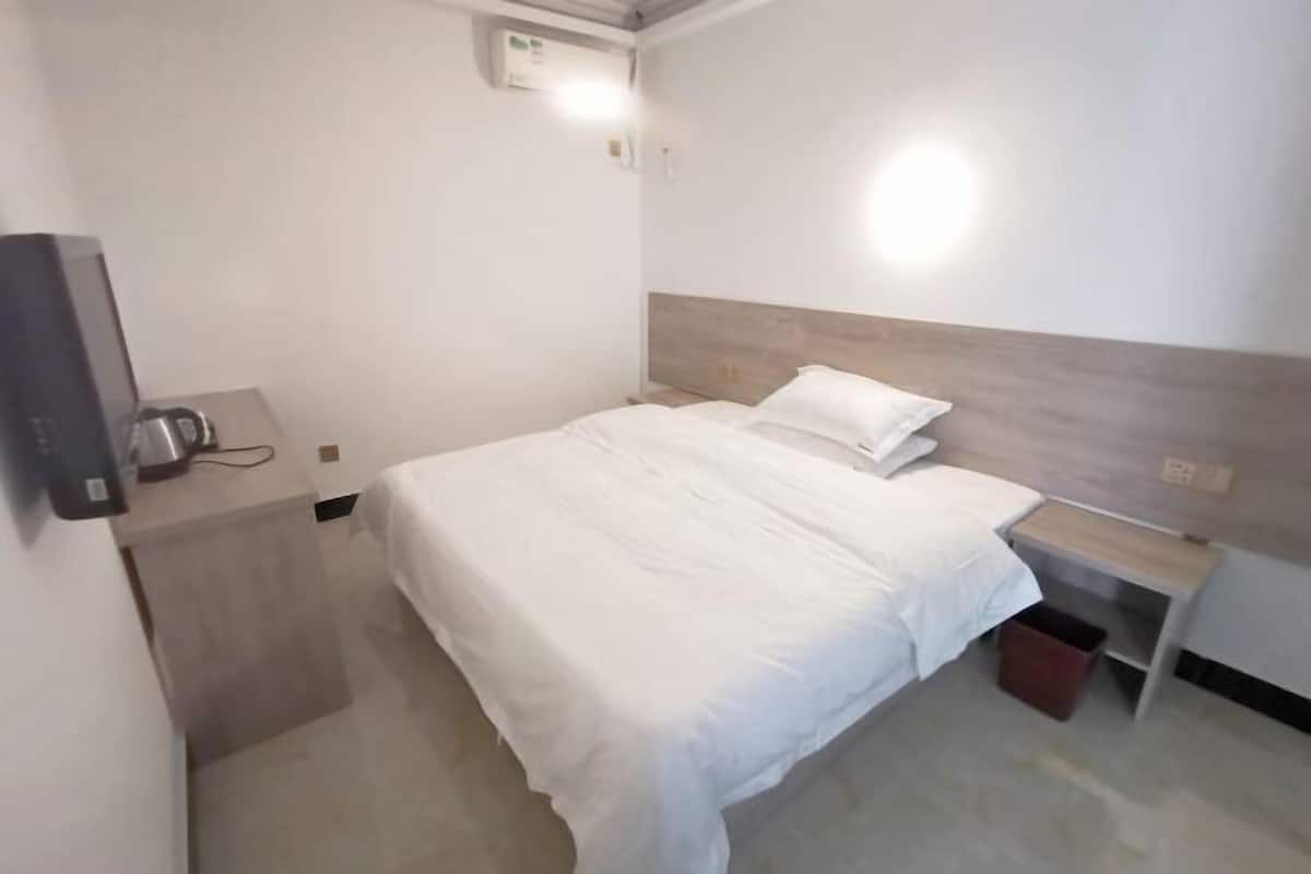 Habitación de hotel pequeña y limpia con una cama individual, una mesita de noche, una papelera y un televisor montado en la pared.