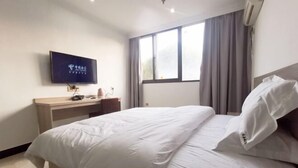 Habitación de hotel con cama, escritorio, televisión y ventana con cortinas.
