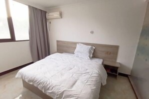A hotel room with a bed, a nightstand, a window with curtains, and an air conditioning unit. - Yujiacheng Hotel (Fuqing)