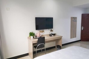 A hotel room with a bed, a desk with a chair, a television, a small plant, and a door. - Yujiacheng Hotel (Fuqing)