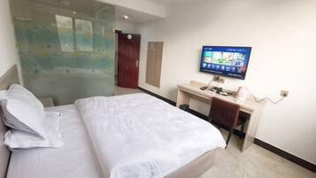 A hotel room with a bed, a desk, a television, and a glass partition.