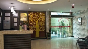 Zona de recepción de hotel con diseño moderno, que incluye un mostrador de recepción, un panel decorativo con motivo de árbol y una gran lámpara de araña.