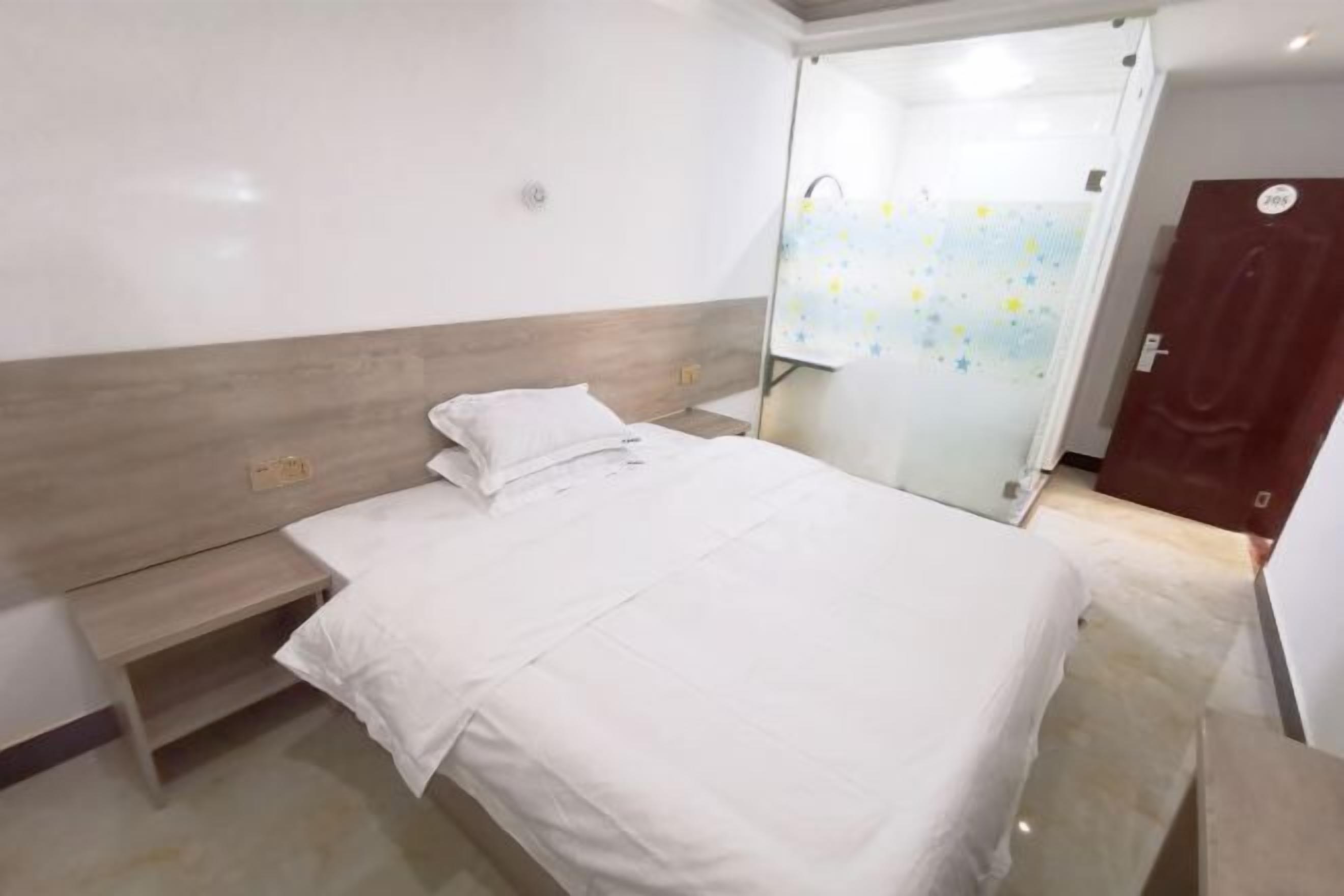 A hotel room with a bed, a bedside table, a small bench, and a door leading to a bathroom.