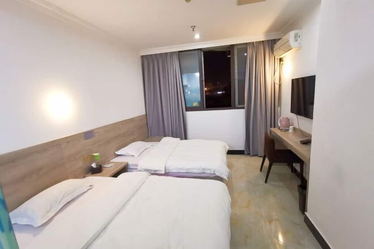 Habitación de hotel con dos camas, un escritorio, una silla, un televisor y un aire acondicionado.