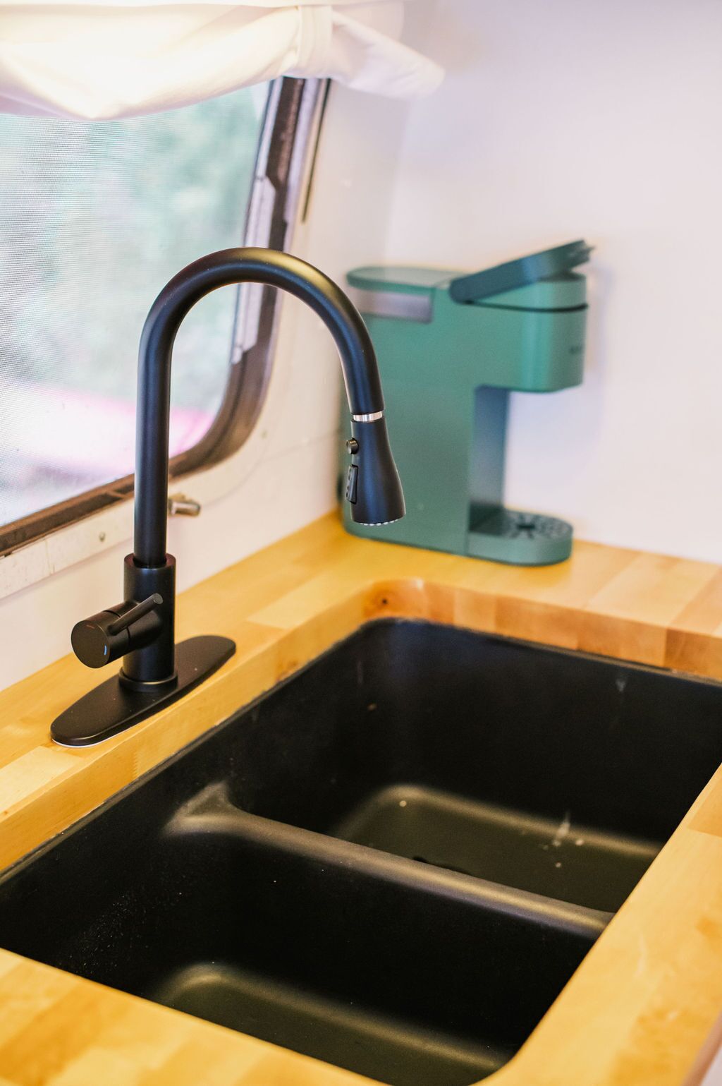 Un évier de cuisine avec un robinet noir et une fenêtre au-dessus.