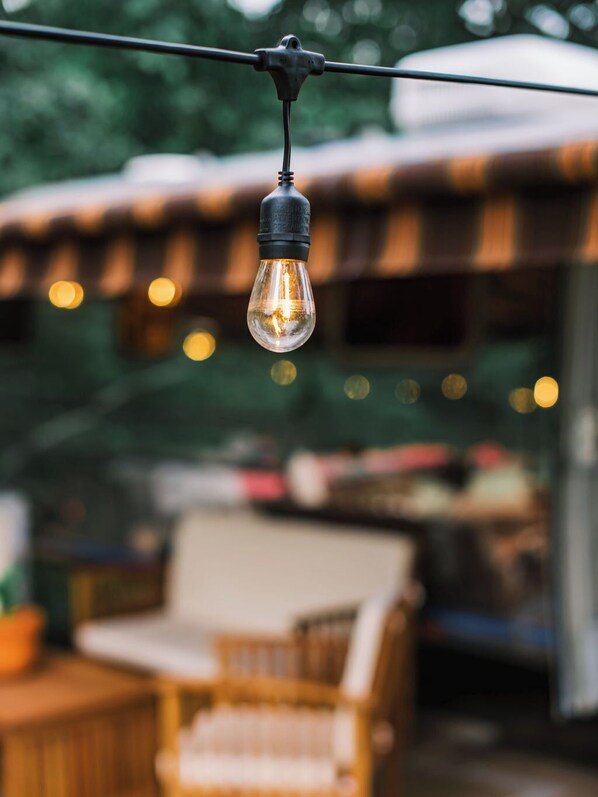 A hanging light bulb in an outdoor setting with a blurred background of a wooden structure and a chair.