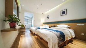 Habitación de hotel con dos camas, piso de madera, planta en maceta y vistas al exterior.