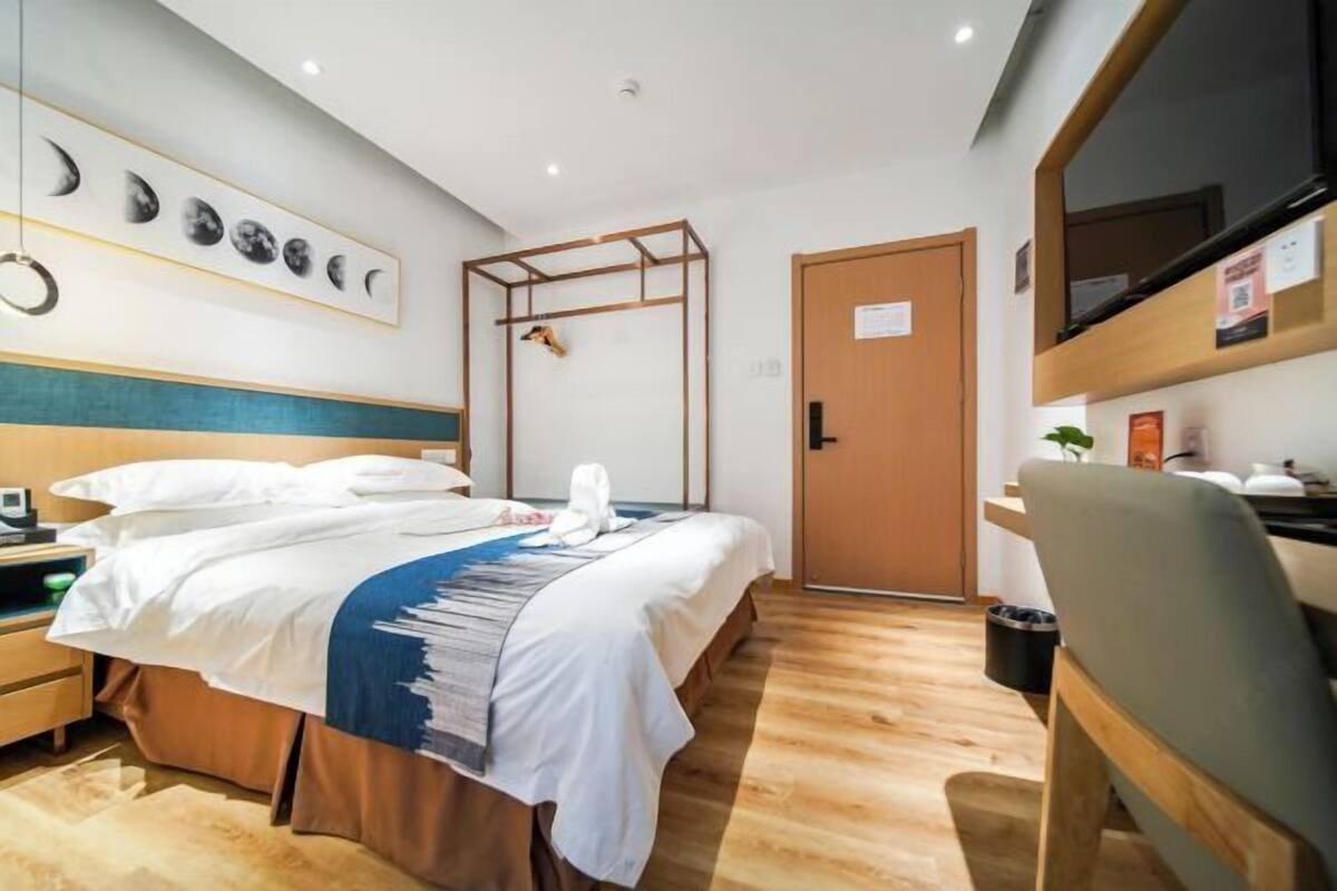 Habitació d'hotel amb un llit, una taula de treball, una cadira, un paviment de fusta, una porta i una paret amb un calendari de fases lunars.