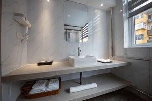 Une salle de bain moderne avec un plan de toilette en marbre, un lavabo blanc, un miroir et un porte-serviettes.