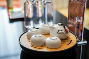 Une collection de théières et de tasses blanches est présentée sur un plateau en bois, et une théière décorative, ornée d’une figurine, attire l’attention.