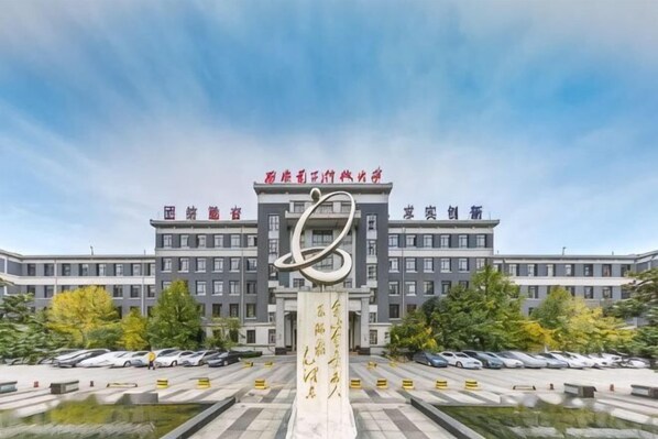 A building with a large central sculpture, multiple parking lots, and a clear sky. - Xidian Hotel (Xi'an University of Electronic Technology Taibai South Road Subway Station) (Xi'an)