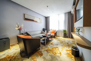 Une chambre d’hôtel moderne, dotée d’un canapé, d’un fauteuil, d’une table basse et d’une grande fenêtre avec des rideaux.