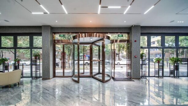 Un vestíbulo con puerta giratoria, ventanas amplias y suelo de mármol.