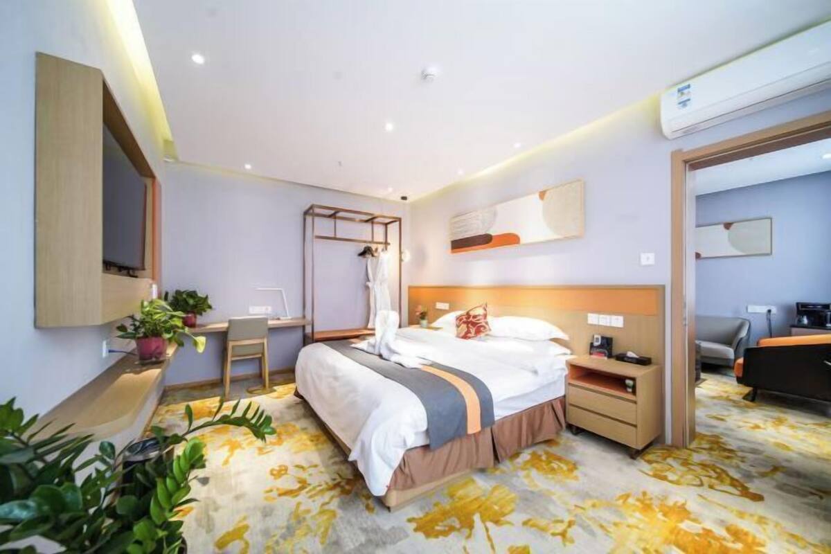Habitació d'hotel amb llit, taula de nit, escriptori, cadira, plantes en maceta i unitat de climatització.