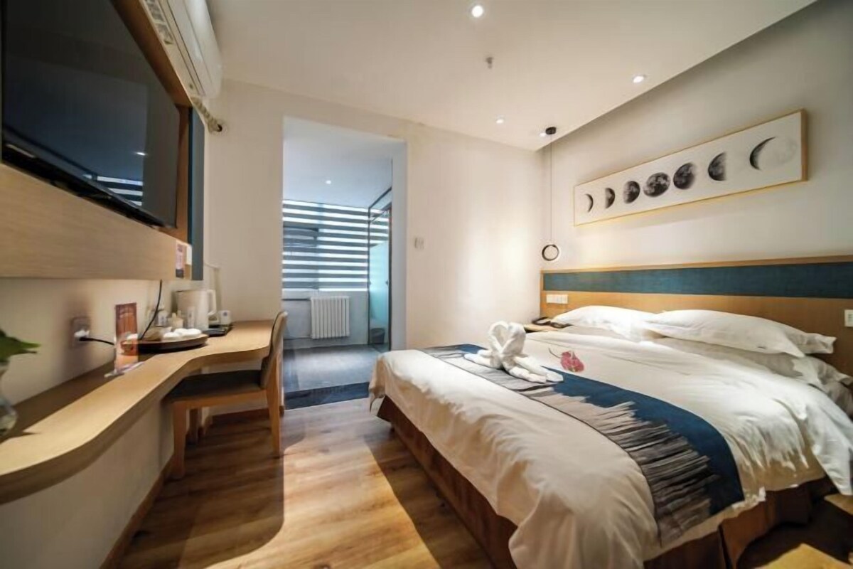Une chambre d’hôtel moderne équipée d’un lit, d’un bureau et d’une œuvre d’art murale représentant les différentes phases de la lune.