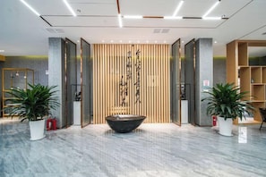 A reception area with a reception desk, a large potted plant, a black water feature, and a wooden wall with vertical lines. - Xidian Hotel (Xi'an University of Electronic Technology Taibai South Road Subway Station) (Xi'an)