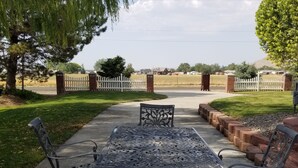 Un patio al aire libre con una mesa y sillas de metal, rodeado por una cerca blanca de piquetes y un muro de ladrillo.