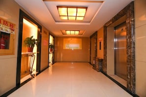 Un couloir d’hôtel avec un sol carrelé, un comptoir de réception, une plante en pot et un ascenseur.