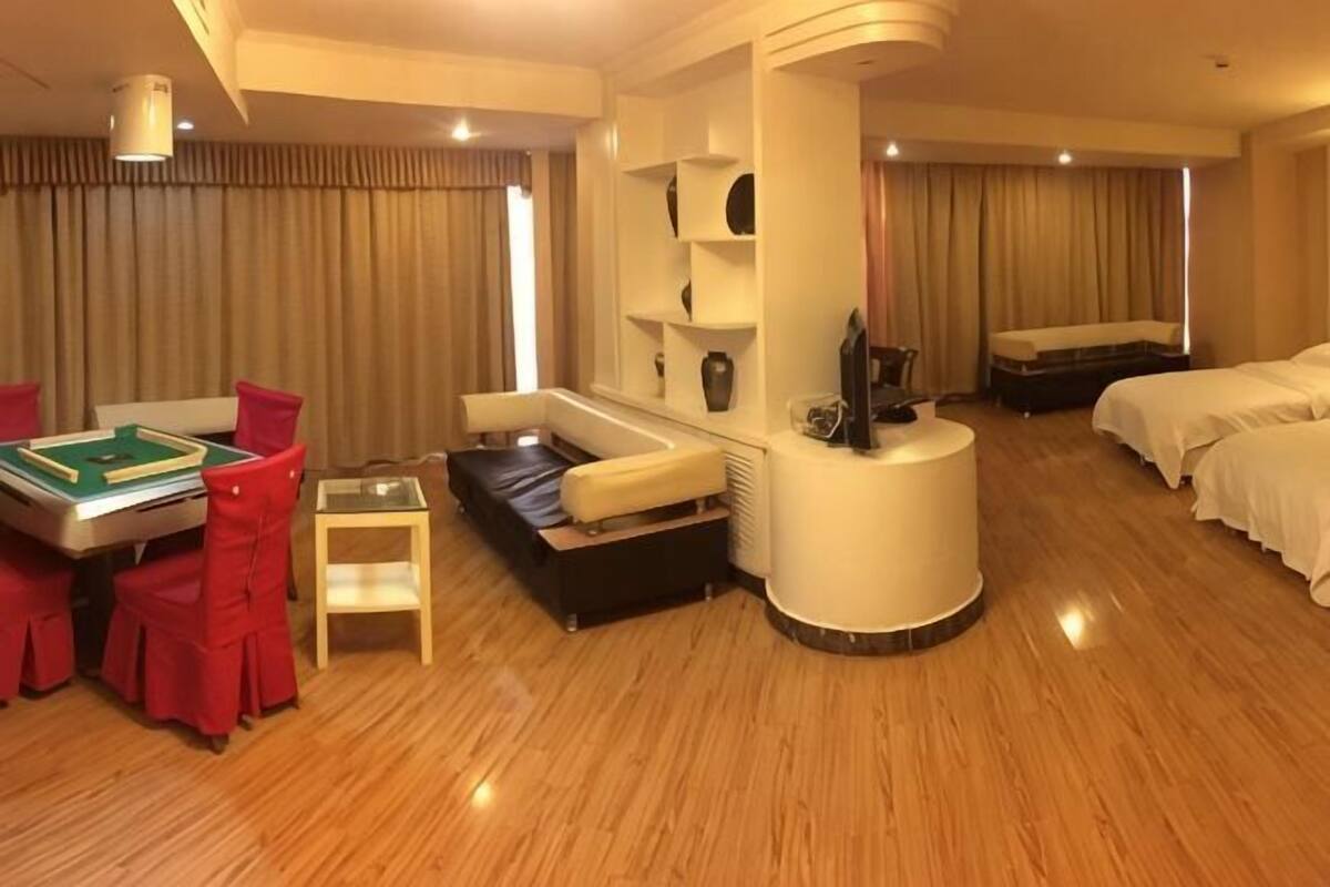 A hotel room with a dining table, red chairs, a sofa, a bed, and a TV.
