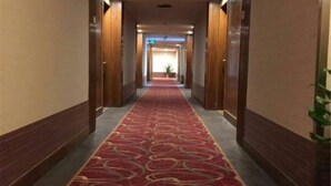 A hotel hallway with a red carpet, wooden walls, and a plant on the right. - Tiandu Hotel (Cixi)