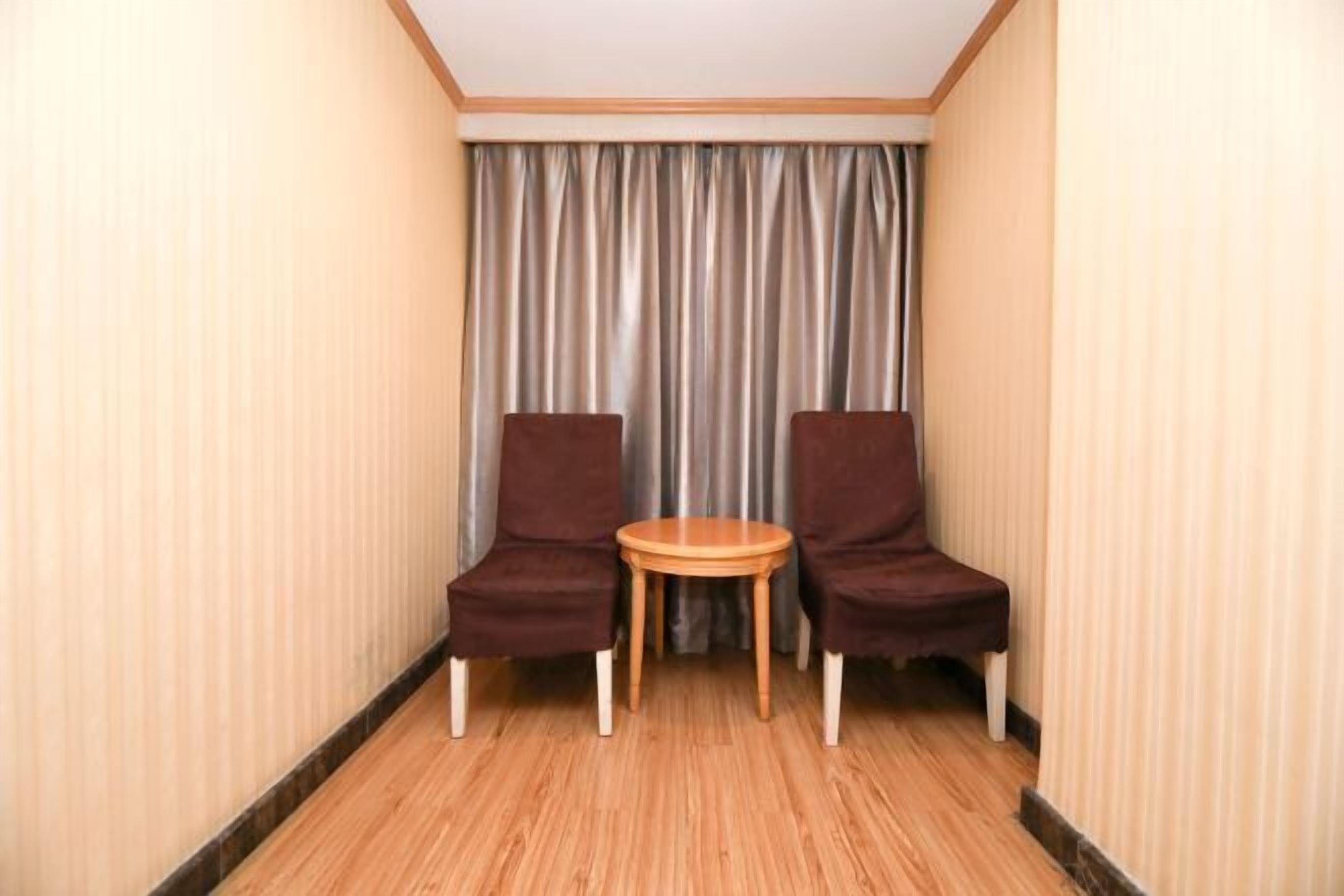 A small room with two brown chairs and a wooden table, a curtain, and striped wallpaper.