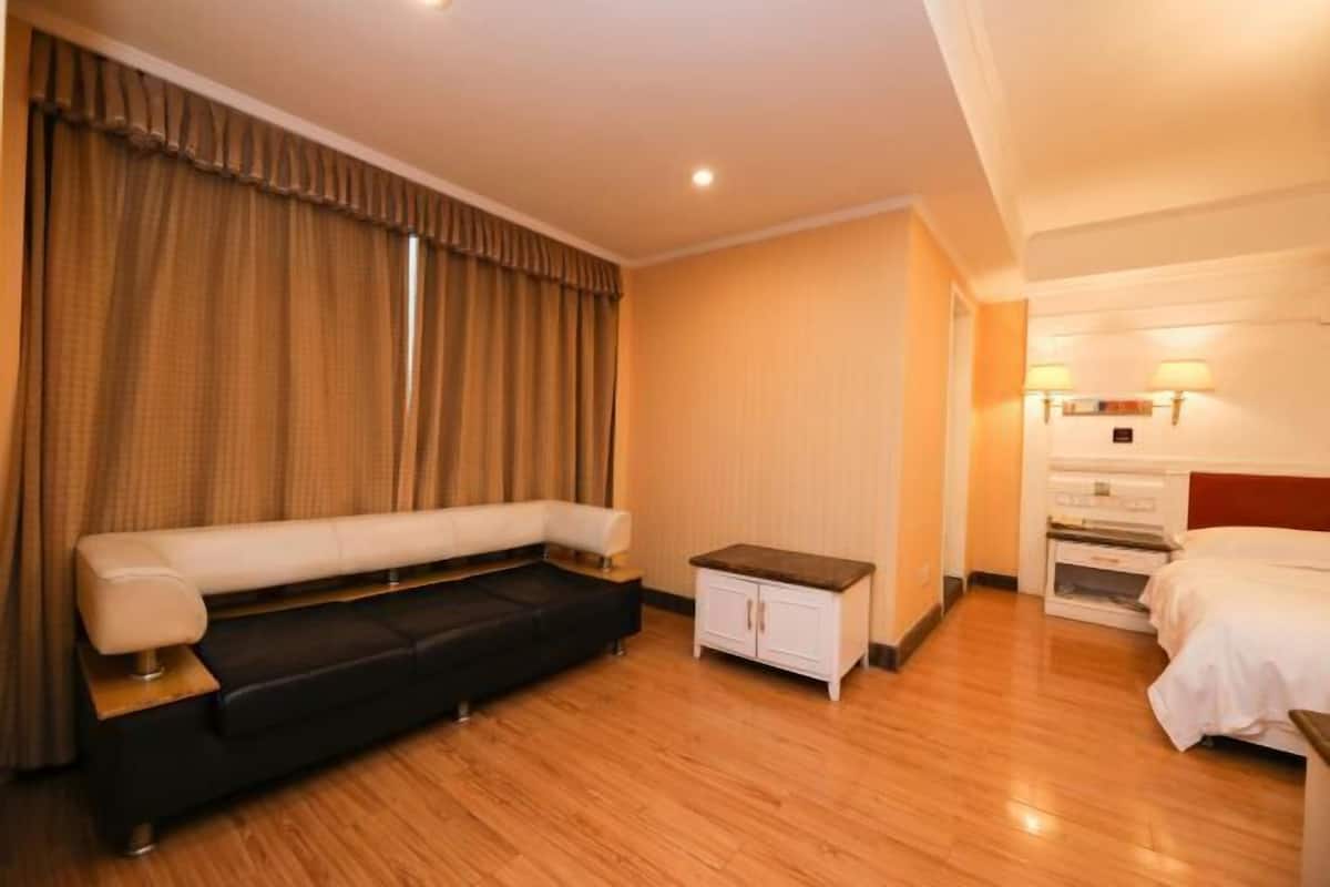 A hotel room with a sofa, a small cabinet, a bed, and a nightstand.