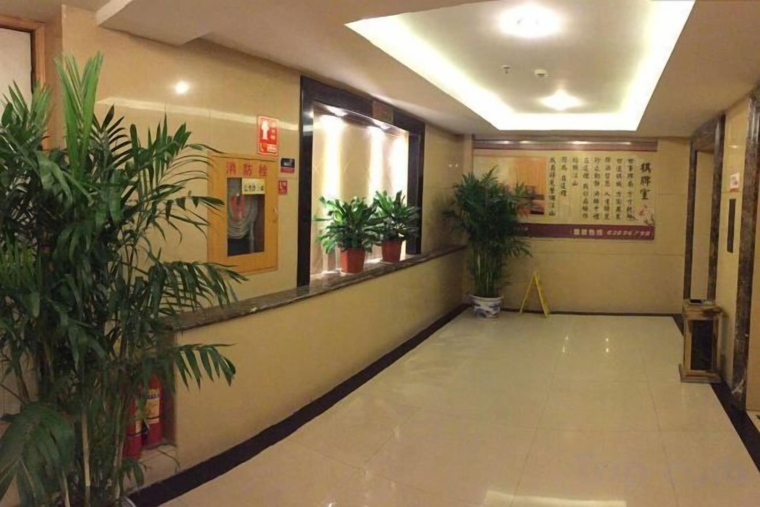 A hotel corridor with potted plants, a fire extinguisher, and a bulletin board.