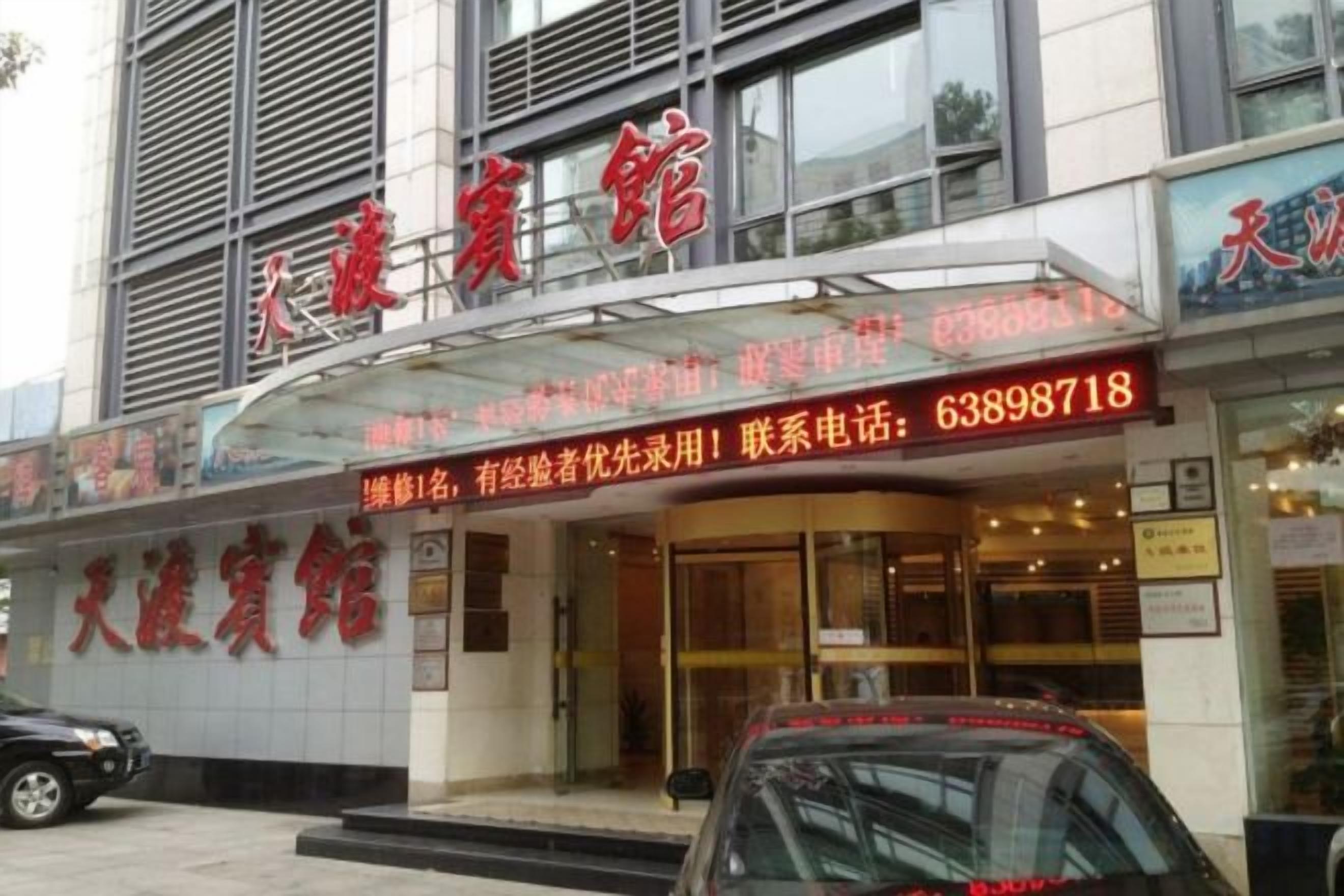 A hotel entrance with a glass canopy, signage, and a contact number.