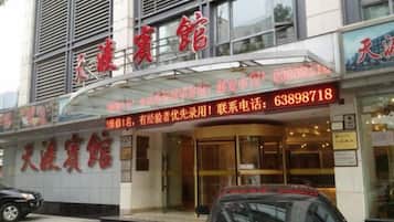A hotel entrance with a glass canopy, signage, and a contact number.