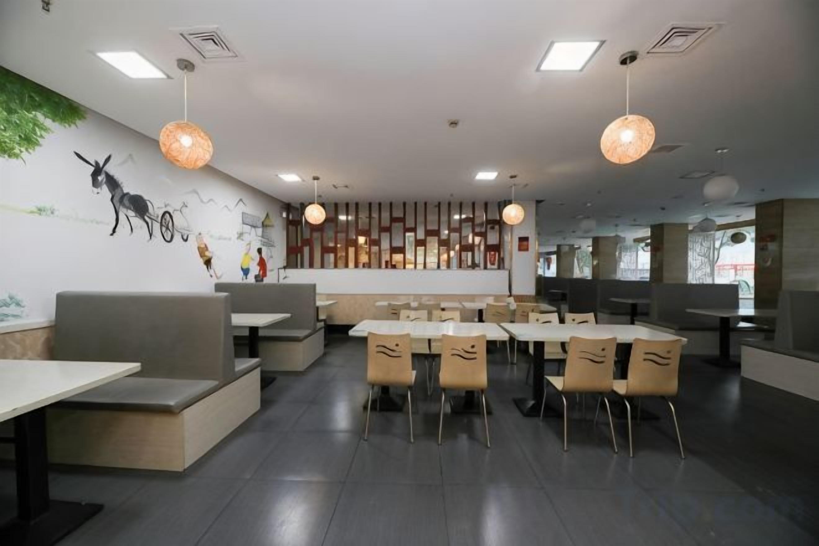 L'intérieur d'un restaurant, avec des banquettes, des tables et des lampes suspendues.