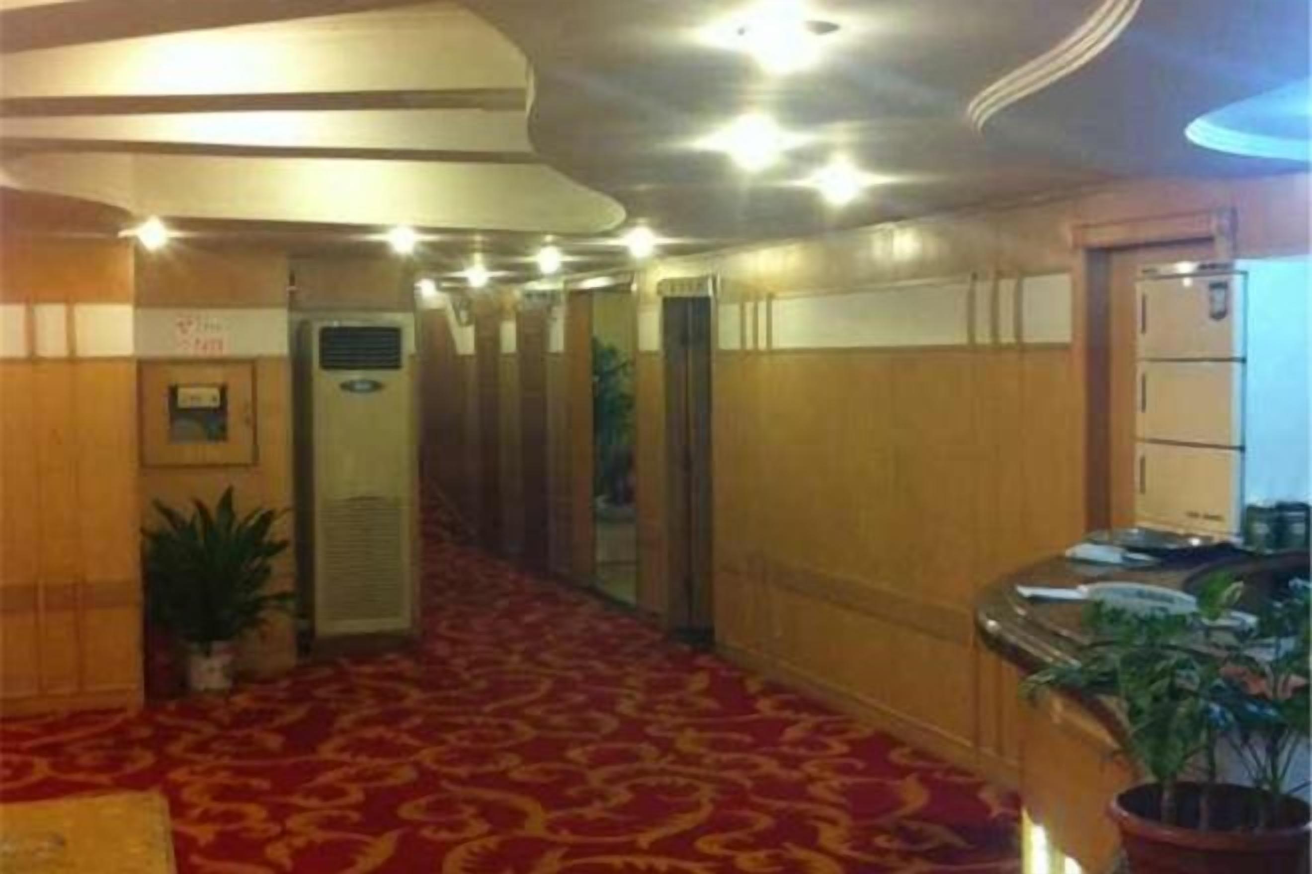Un couloir d’hôtel avec un tapis rouge, des murs en bois et un comptoir de réception agrémenté d’une plante.