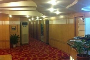 Een hotelgang met een rood tapijt, houten wanden en een receptiebalie met een plant.