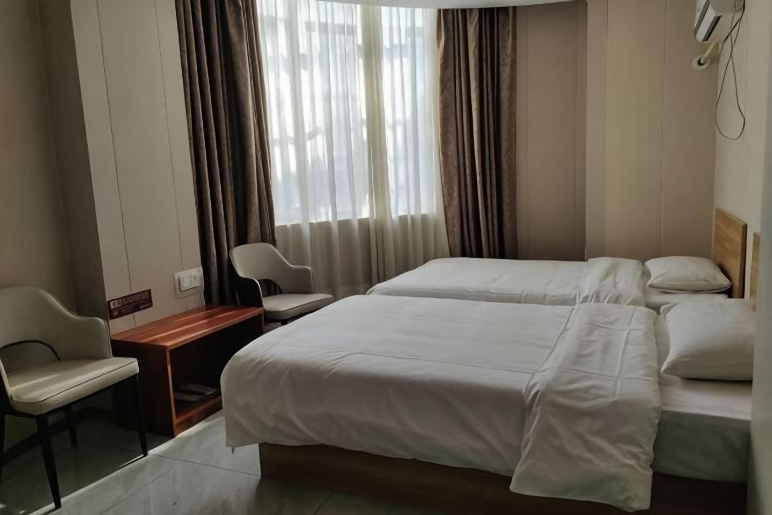 Una habitación de hotel con dos camas, un escritorio, una silla y una ventana con cortinas.
