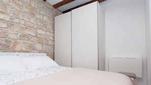 A bedroom with a stone wall, a bed with patterned bedding, and a white wardrobe.
