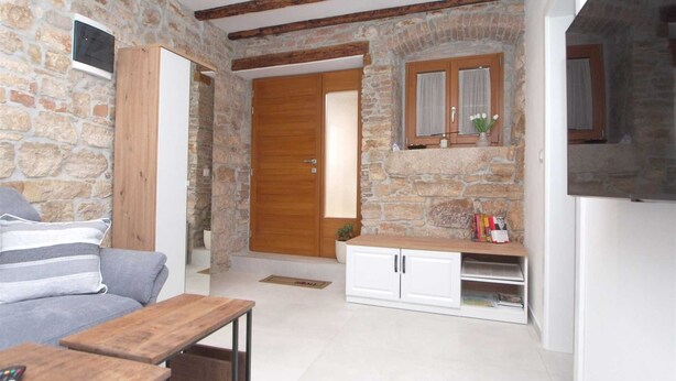 A cozy room with stone walls, a wooden door, a small cabinet, and a TV.