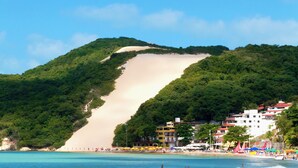 Una playa con una duna de arena, sombrillas y edificios a lo largo de la costa.