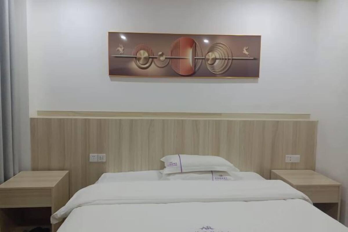 Une chambre d’hôtel comprenant un lit, deux tables de chevet, une œuvre d’art accrochée au mur et une tête de lit en bois.