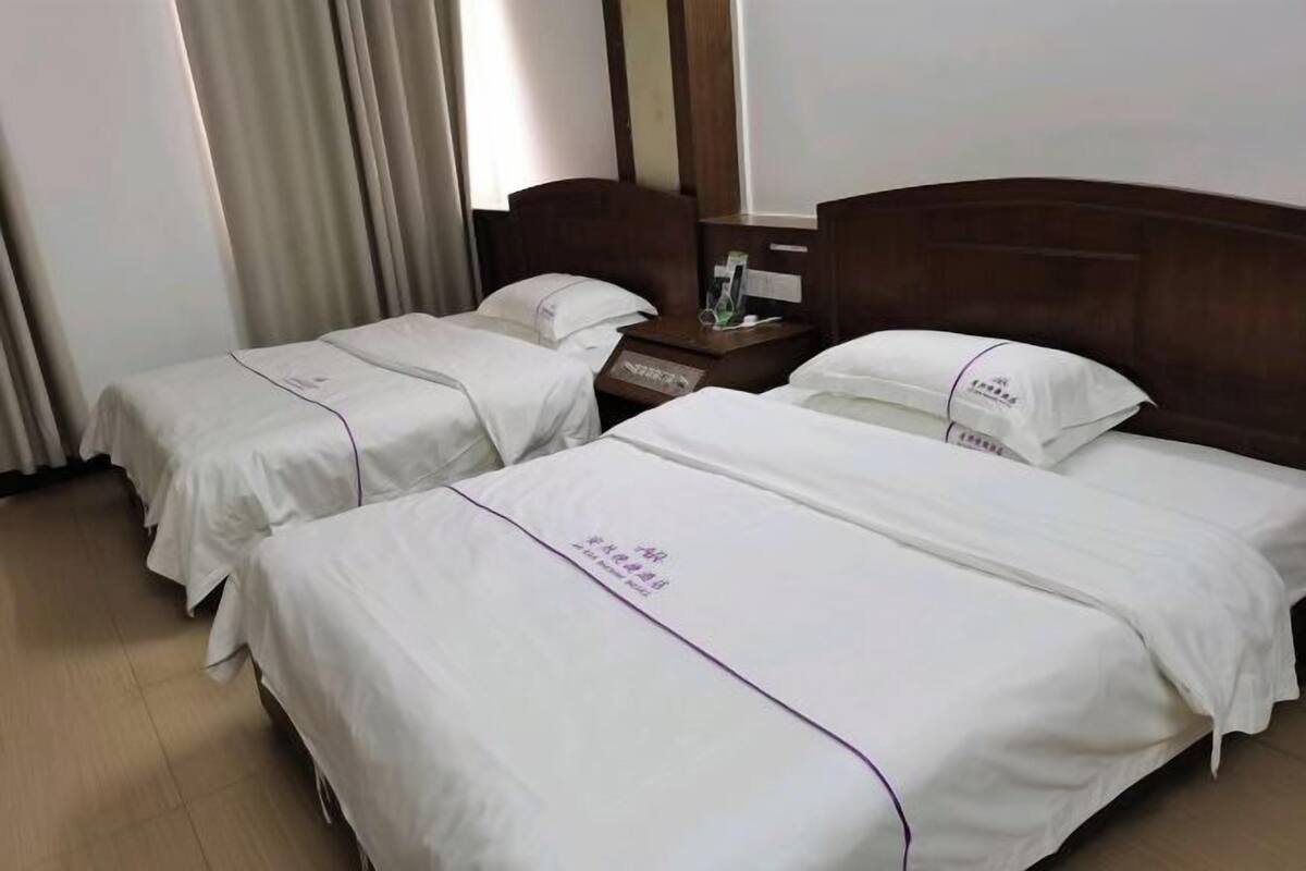 Une chambre d’hôtel avec deux lits, une tête de lit en bois, une table de chevet et une fenêtre avec des rideaux.