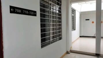 A corridor with a door marked with numbers 708 and 718-728, a window with a metal grid, and a tiled floor.