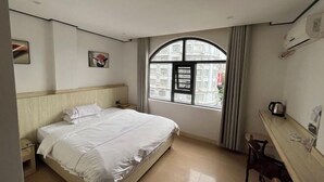 Une chambre d’hôtel équipée d’un lit, d’un bureau, d’une chaise, d’une fenêtre avec des rideaux et d’un appareil de climatisation.