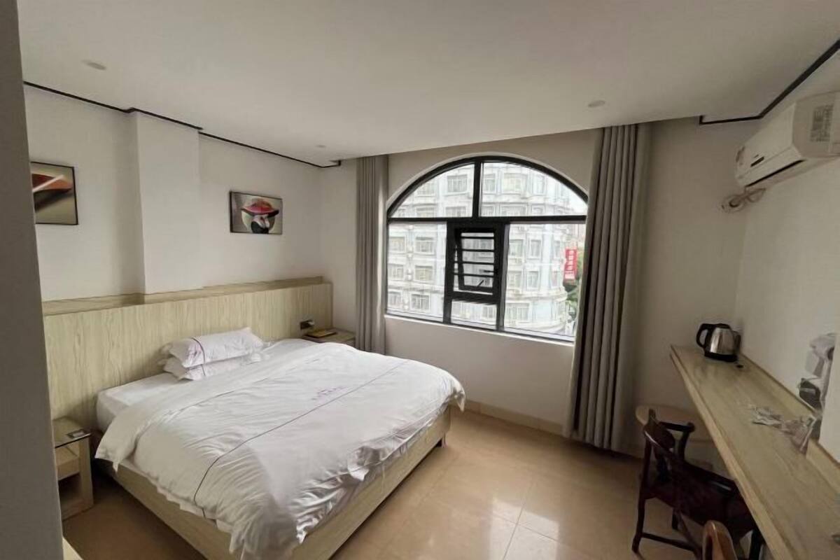 Une chambre d’hôtel équipée d’un lit, d’un bureau, d’une chaise, d’une fenêtre avec des rideaux et d’un appareil de climatisation.