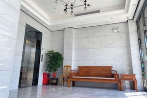 Un vestíbulo con piso de mármol, un banco de madera, una planta en maceta y un objeto rojo.