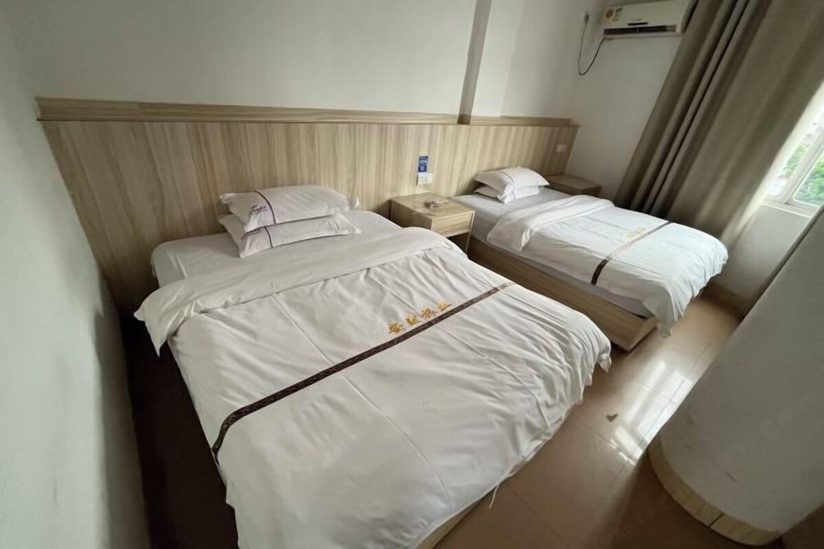 A hotel room with two beds, a wooden headboard, a nightstand, and an air conditioning unit.